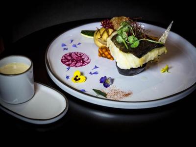 Elegantes Dessert mit Schokolade und essbaren Blüten auf weißem Teller neben einer kleinen Tasse.