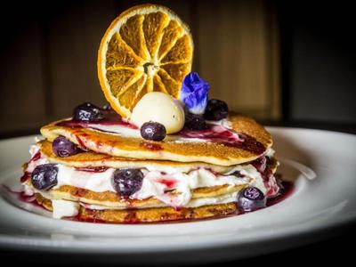 Ein gestapelter Pfannkuchen mit Beeren, Sahne, Butter und einer getrockneten Orangenscheibe.