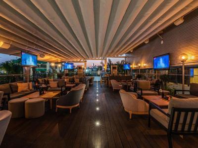Gemütliche Hotelbar mit warmem Licht, Sesseln und Fernsehern unter einer Falten-Decke.