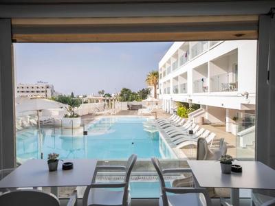 Moderner Hotelpool mit Liegestühlen und weißen Gebäuden an einem sonnigen Tag.