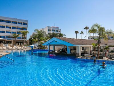 Großer Außenpool mit Swim-up-Bar neben Hotels unter blauem Himmel und Palmen.