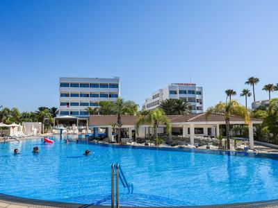 Großer Outdoor-Pool vor modernen Hotelgebäuden mit Palmen und blauem Himmel.