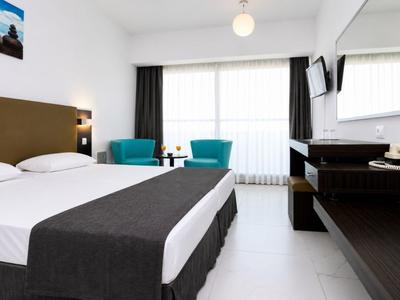 Helles Hotelzimmer mit Doppelbett, zwei blauen Sesseln und großem Fenster mit Vorhängen.