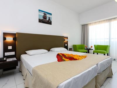 Hell eingerichtetes Hotelzimmer mit Doppelbett, Sitzbereich und großen Fenstern.