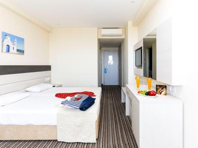 Hell eingerichtetes Hotelzimmer mit Doppelbett, TV und moderner Einrichtung.