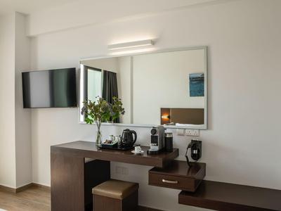 Moderner Hotelzimmer-Schreibtisch mit Fernseher, Spiegel und Kaffeemaschine an weißer Wand.