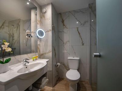 Moderne Hotelbadezimmer mit Marmorfliesen, Waschbecken, Toilette und beleuchtetem Kosmetikspiegel.