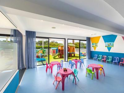 Bunter Kinderspielraum mit kleinen Tischen und Stühlen nahe Fensterwand in hellem Raum.