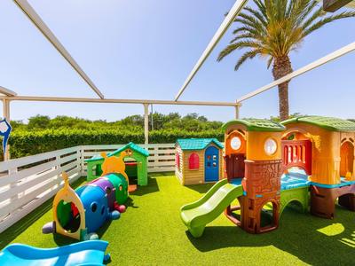Kinder-Spielplatz mit bunten Rutschen, Klettergerüsten und grünem Kunstrasen unter blauem Himmel.
