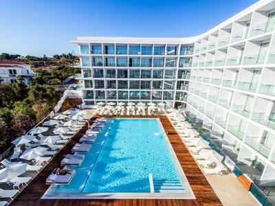 Moderner Hotelpool mit Sonnenliegen und Glasfassade, sonniger Himmel im Hintergrund.