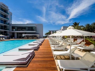 Moderner Hotelpool mit weißen Liegen und Sonnenschirmen unter blauem Himmel.