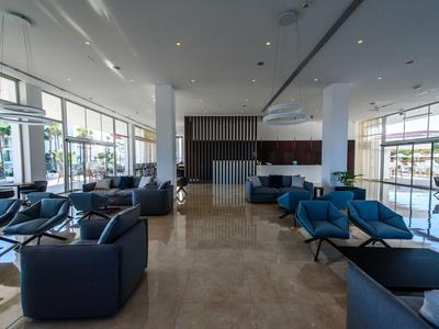 Moderne Hotellobby mit blauen Sesseln, großen Fenstern und glänzendem Marmorboden.