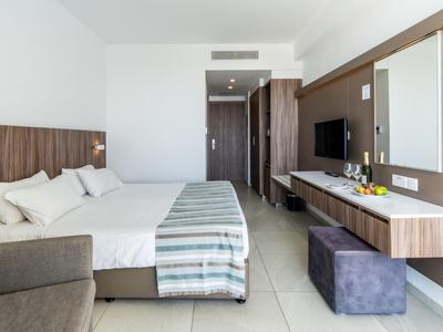 Modernes Hotelzimmer mit Doppelbett, Fernseher, Sitzbereich und großer Spiegelwand.