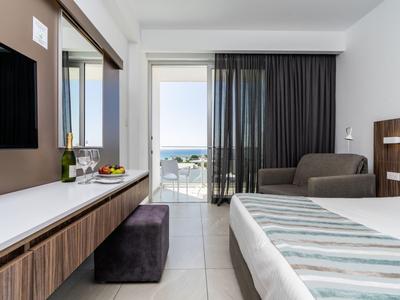 Modernes Hotelzimmer mit Bett, Sitzbereich und Balkon mit Meerblick.