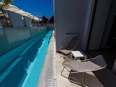 Enge Terrasse mit schmalem Pool und zwei Liegestühlen neben einem weißen Gebäude.