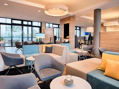 Mobili moderni per lounge d'hotel con poltrone blu, divani grigi e cuscini gialli in una stanza luminosa.