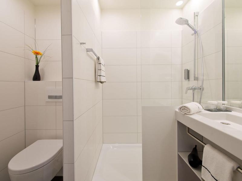 Salle de bain moderne compacte avec carrelage blanc, douche à l'italienne, toilettes et lavabo.