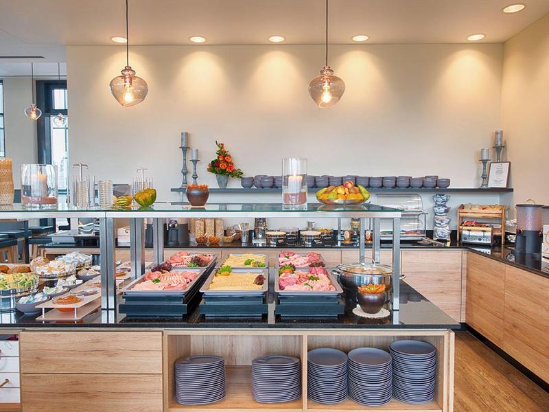 Espace petit-déjeuner d'hôtel moderne avec pâtisseries variées, fruits et éclairage moderne