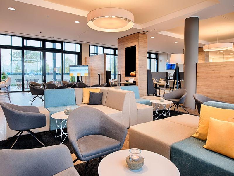 Salon d'hôtel moderne avec canapés bleus et gris, grandes fenêtres et décoration en bois.