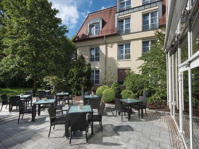 Hotel terrace with tables and chairs beside a building and trees in the background.
