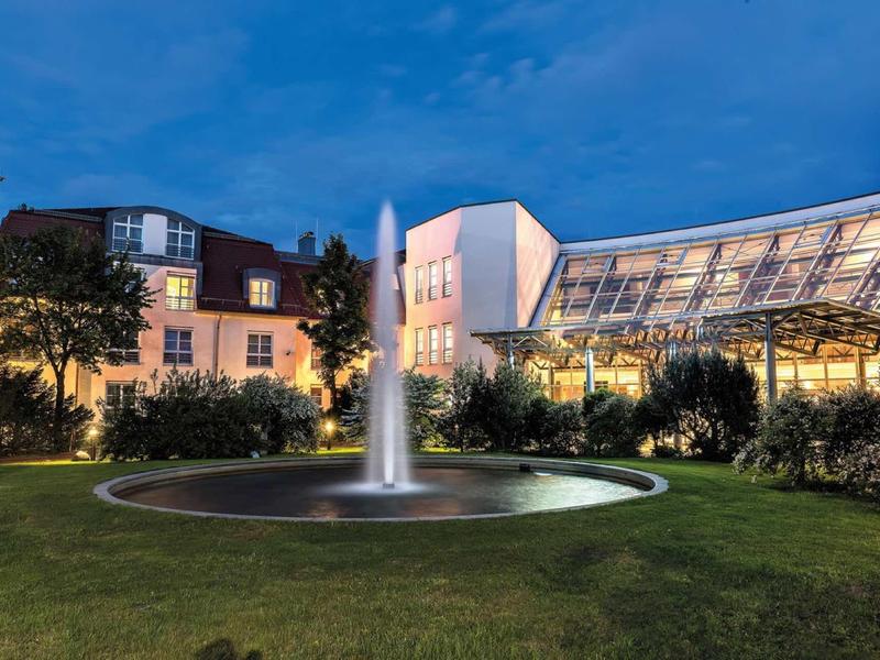 Hotel building with modern glass facade and illuminated fountain in garden at night