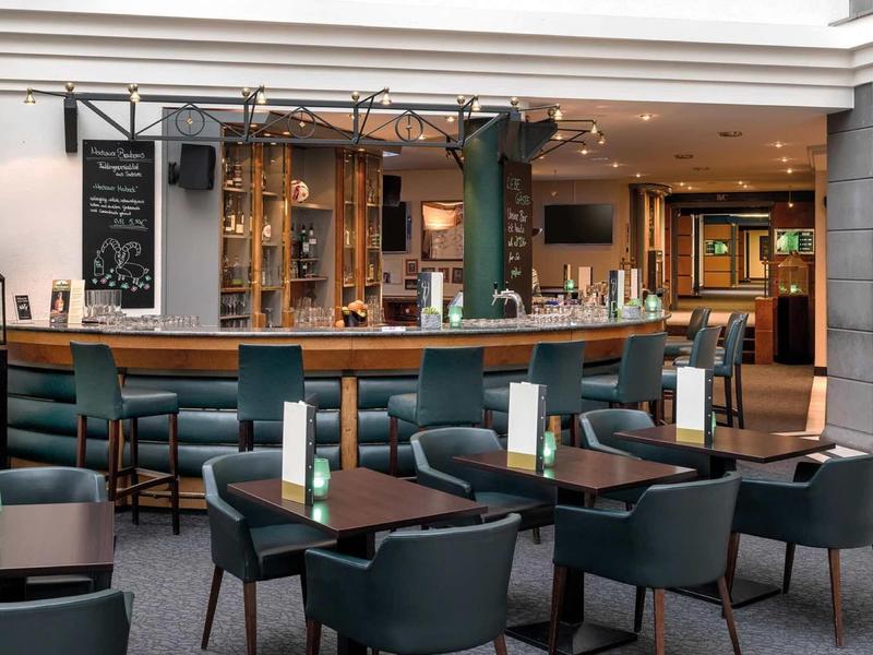 Cozy bar with dark chairs, tables, and a well-stocked counter in a hotel.