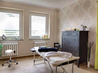 Lichte behandelkamer met behandelbank, kast en planten.