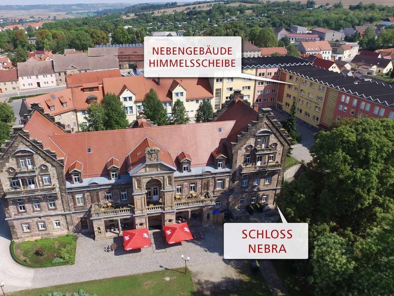 Vogelvlucht van een historisch kasteel met aangrenzende gebouwen in een groene stadsomgeving.