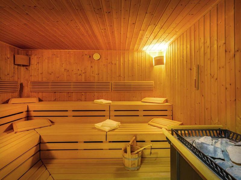 Houten sauna met bankjes, emmer en zandloper, verlicht met warm licht.