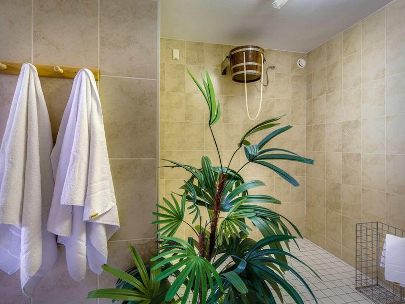 Saunaruimte met houten emmer, witte handdoeken en groene planten in een lichte ruimte.