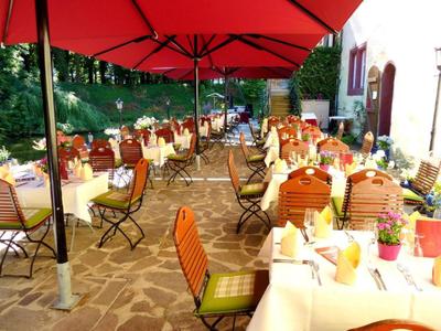 Terrasse eines Restaurants mit Tischen, Stühlen und roten Sonnenschirmen im Freien.