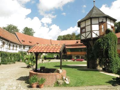 Innenhof eines Fachwerkhauses mit Brunnen, Rasen und einem turmähnlichen Bauwerk mit Pflanzen.