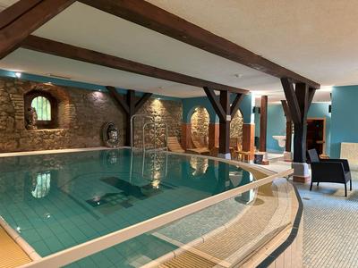 Hallenbad mit Steinwänden, Holzbalken und Sitzgelegenheiten neben dem Becken.