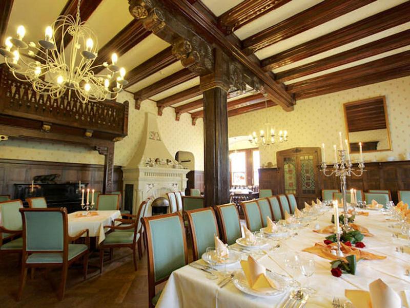 Elegantní jídelna s dřevěnými trámovými stropy, velkými stoly a dekorativním osvětlením.