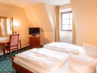 Helles Hotelzimmer mit zwei Einzelbetten, Schreibtisch, TV und Fenster.