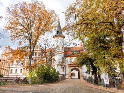 Historic building with tower and archway among trees in autumn.