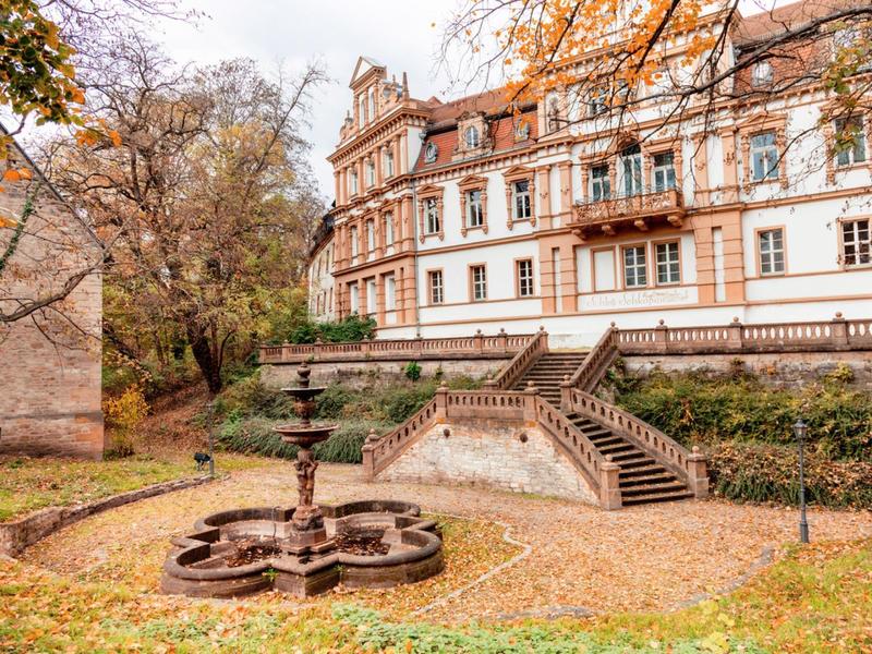 A historic building with a garden and fountain area in autumn.