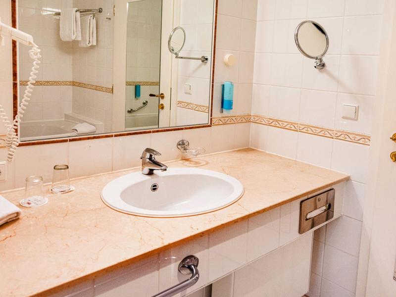 Bright hotel bathroom with sink, large mirror, and wall-mounted hairdryer.
