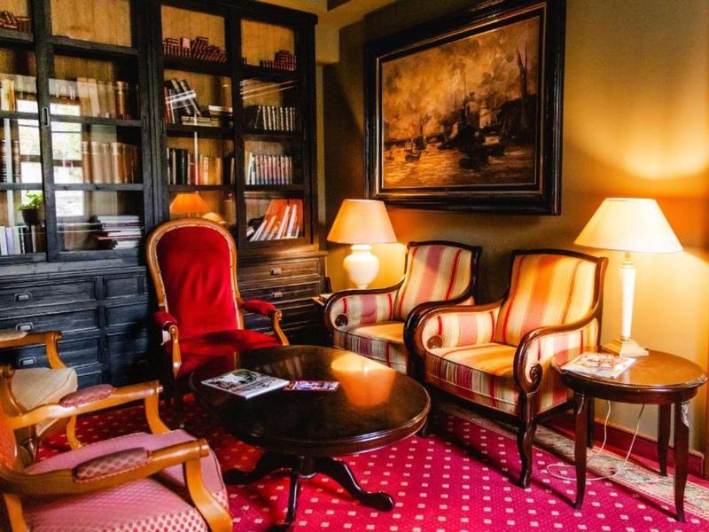 Cozy hotel reading lounge with red patterned carpet, classic armchairs, and bookshelves.