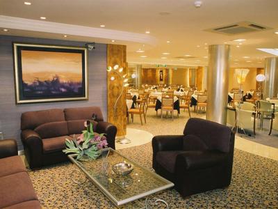 Un salon d'hôtel élégamment meublé avec des fauteuils, des canapés et une salle à manger en arrière-plan.