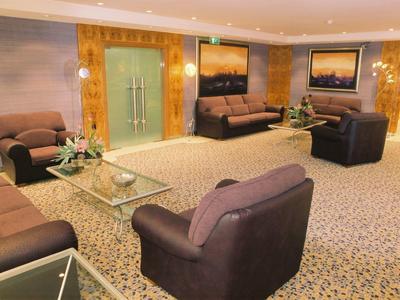 Salon d'hôtel confortable avec canapés, fauteuils et tables basses en verre sur moquette.