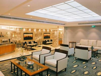 Salon d'hôtel lumineux avec fauteuils modernes, tables et panneau de plafond éclairé.