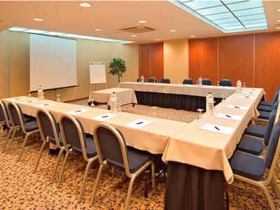 Salle de conférence avec tables en U et chaises, projecteur et éclairage de plafond.