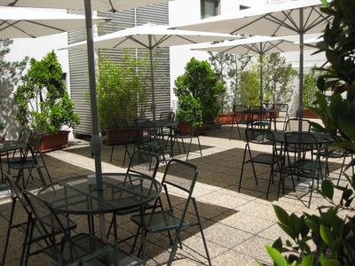 Espace extérieur ensoleillé avec tables, chaises et parasols à côté d'un bâtiment hôtelier.