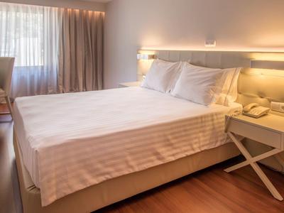 Chambre d'hôtel confortable avec grand lit, table de chevet et rideau clair à la fenêtre.