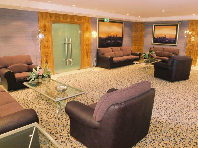 Salon d'hôtel confortable avec canapés, fauteuils et tables basses en verre sur moquette.