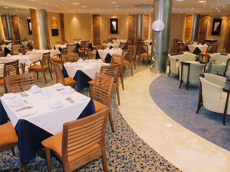 Restaurant d'hôtel élégant avec tables dressées et chaises en bois sous un éclairage chaleureux.