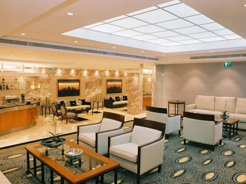 Salon d'hôtel lumineux avec fauteuils modernes, tables et panneau de plafond éclairé.