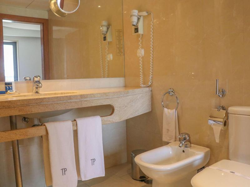 Salle de bain d'hôtel lumineuse avec lavabo, bidet, toilettes et serviettes sous le comptoir.