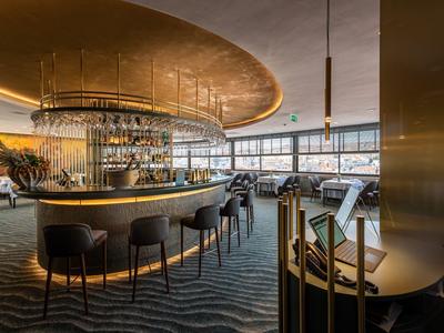 Elegante hotelbar met ronde bar, comfortabele stoelen en groot raam met uitzicht op de stad.